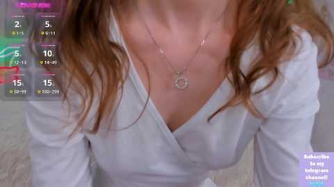 Media: A video of a woman with light skin, wearing a white blouse and a silver necklace, indoors with blurred background.