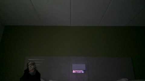 Media: A dimly-lit video of a woman with long hair and glasses standing in a dimly-lit room, looking at a glowing red \"EXIT\" sign on a white wall.