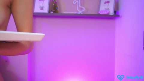 Media: Video of a woman's bare buttocks and thighs, viewed from behind, in a pink-lit room with a white shelf holding decorative items.