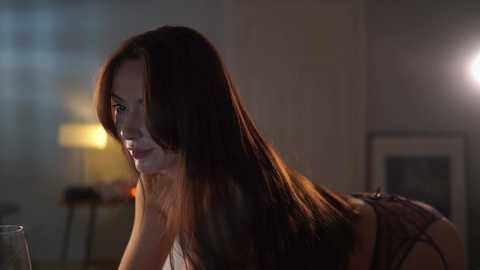 Media: Video of a slender, fair-skinned woman with long, straight brown hair, wearing black lingerie, lying on a bed with dim lighting, creating a moody, intimate atmosphere.