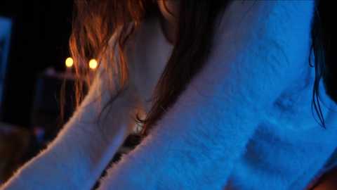 Media: Video of a woman with wet, tousled hair, wearing a light blue, fluffy bathrobe, holding her head, illuminated by blue light, in a dimly lit bathroom.