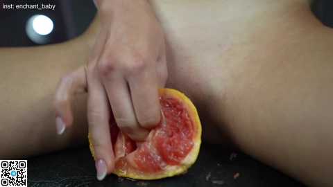 Media: Video of a light-skinned person, possibly female, with their legs spread and a hand holding a grapefruit, revealing the juicy, pink flesh. The background is blurred, and the image includes a QR code in the bottom left corner.