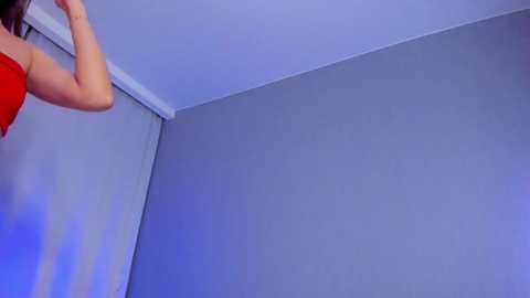 Media: Video of a woman in a red tank top, partially visible, standing in a corner room with light blue walls.