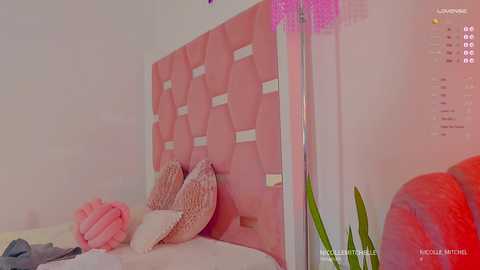 Media: Video of a modern bedroom with a pink, hexagonal-patterned headboard, textured pillows, a red couch, and a tall purple lamp. The room is bright and cozy, with soft pink lighting.