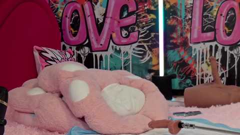 Media: Video of a pink plush bed with white spots, surrounded by graffiti wall art and colorful pillows, featuring the word \"LOVE\" prominently.