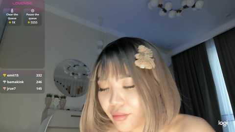 Media: Video of an Asian woman with shoulder-length, straight hair, wearing a cream-colored headband, in a dimly lit room with a mirror and window.