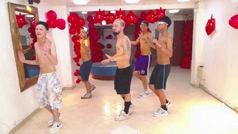 Media: Video of shirtless men in workout gear practicing boxing in a gym with red balloons and heart decorations on white walls.