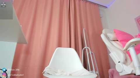 Media: Video of a cozy, minimalist bedroom with a white chair, pink curtains, a metal standing lamp, and a pink rocking chair.