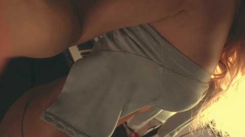 Media: A close-up video of a woman's buttocks, wearing light gray shorts, with her long, wavy hair visible. The background is blurry, suggesting an indoor setting with warm lighting.