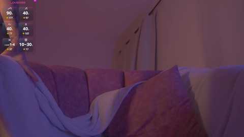 Media: Video of a dimly lit bedroom with a white bed covered in a purple duvet. A white dresser with drawers is visible in the background. A smartphone screen displays weather and temperature information.