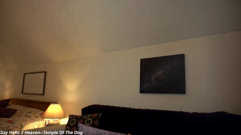 Media: A video of a dimly lit bedroom with a wooden bed, a nightstand lamp, a framed picture, and a large dark painting on the wall.