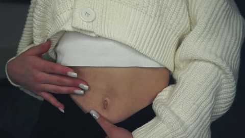 Media: Video of a light-skinned person with a white sweater, exposing a bare stomach, with manicured nails painted silver.