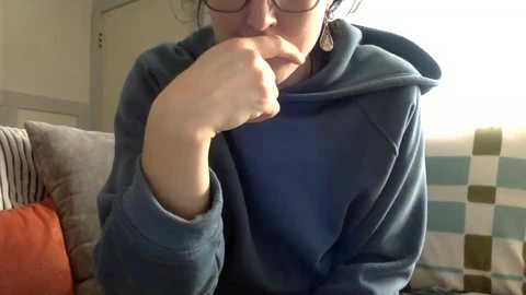 Media: A video shows a woman with glasses, wearing a blue hoodie, sitting indoors, with a checkered blanket in the background and striped cushions.