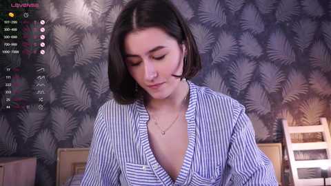 Media: Video of a young woman with straight black hair, wearing a loose, blue and white striped robe, in a bedroom with patterned wallpaper.