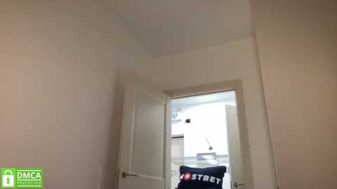 Media: Video of a narrow, empty hallway with white walls and a partly open door leading to a white room with a \"NYST\" pillow.