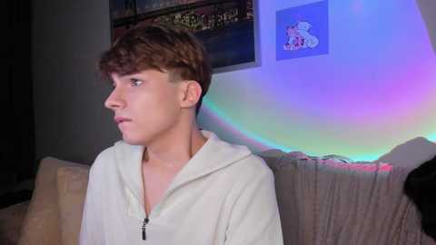 Media: A video of a young boy with short brown hair in a white hoodie, sitting indoors, with a colorful LED light strip in the background.