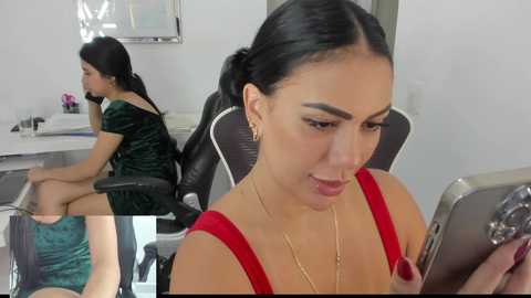 Media: Video of a young woman with dark hair in a red dress, seated in a modern office chair, intently reading a tablet. Background features a white wall with a desk and plants.