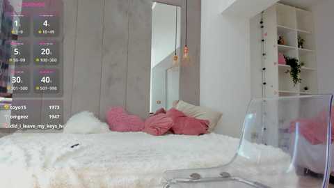 Media: A video of a modern, minimalist bedroom featuring a plush white bed with pink pillows, surrounded by light gray walls, a white bookshelf, and a transparent chair.