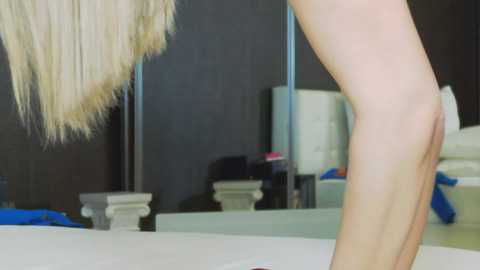 Media: A video captures a blonde woman's leg, partially nude, standing beside a modern bathtub. The background features a sleek, dark bathroom with a white tufted headboard, a blue towel, and a mirror.