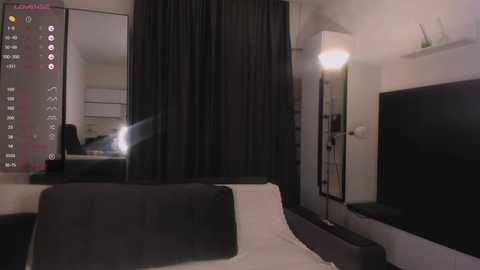 Media: Video of a modern hotel room with a large flat-screen TV, black curtains, white bed, and a contemporary wall-mounted lamp.