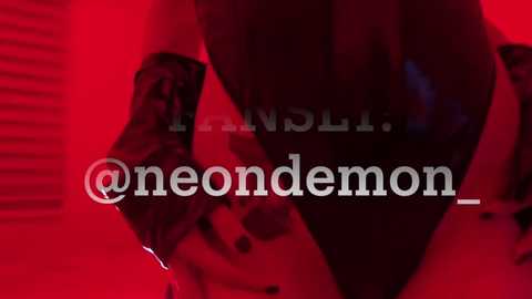 Media: Video of a person in a red-lit room, holding a knife. The image is blurred with the text \"@neondemon\" overlaid. The person's body is partially visible, emphasizing the knife's sharp edge.