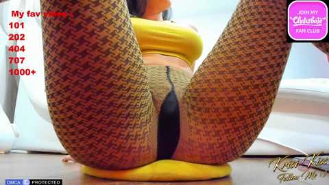 Media: Video of a woman in houndstooth-patterned leggings and a yellow crop top, sitting on a yellow cushion. Background features a white chair. Text overlay mentions \"My fav movie\" and \"1010 votes.\