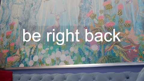 Media: Video of a vibrant, large-scale mural featuring colorful, stylized flowers and a deer in a whimsical, ethereal garden. Text overlay reads \"be right back\" in white, modern font.