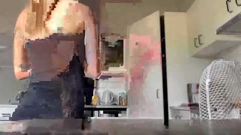 Media: A blurred video of a man in a black tank top, standing in a modern kitchen with white cabinets, a white chair, and a stove in the background.