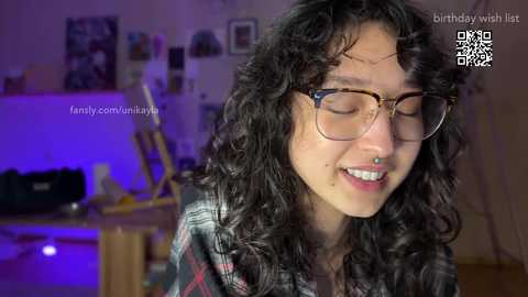 Media: Video of a young woman with curly black hair, wearing glasses, smiling, in a dimly lit room with a birthday wish overlay.
