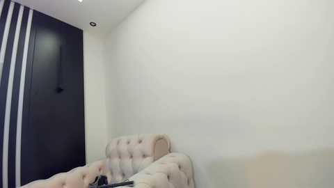 Media: A video of a minimalist bedroom corner with beige tufted sofa, white walls, and a black vertical striped curtain. The room features a modern, clean design.