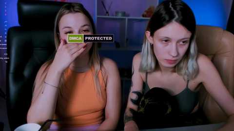 Media: Video of two young women in a dimly lit room, one covering her mouth, the other holding a black cat.