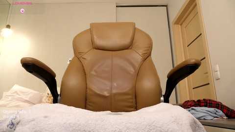 Media: A video of a beige leather office chair with armrests in a modern, sparsely decorated room with a closed door and a partially visible window.
