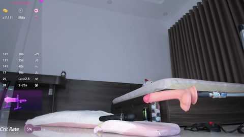 Media: A video shows a modern bedroom with a bed, a nightstand, and dark curtains, featuring a pink dildo on a bed sheet.