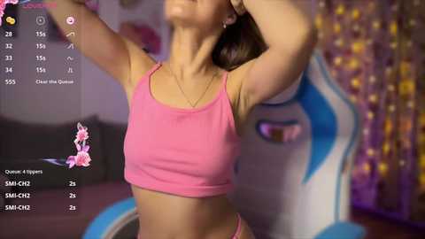 Media: A blurred video of a woman in a pink crop top, arms raised, in a room with a blue unicorn statue and fairy lights.