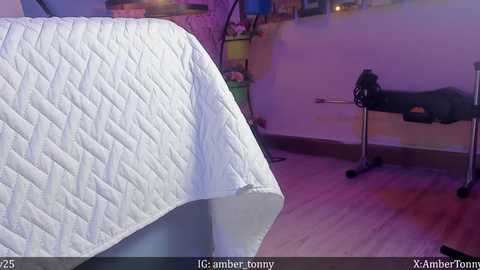 Media: Video of a white quilted bedspread draped over a massage table in a softly lit room with a purple hue.