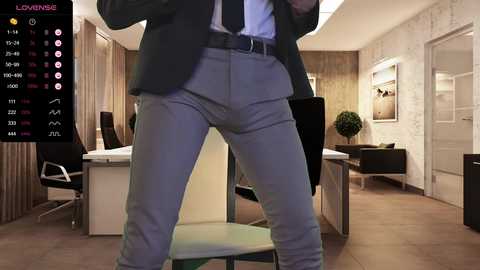 Media: Video of a stylishly dressed man in a suit and tie standing confidently in a modern office. The background features a sleek, minimalist decor with white walls and wooden flooring.