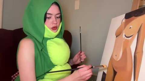 Media: A video shows a woman in a green, hooded costume painting a cartoon character on a canvas, with a yellow shirt and a brush in her hand.
