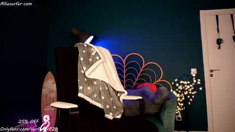 Media: Video of a dark teal bedroom with a starburst headboard, a draped American flag, and a surfboard, featuring a white door and a red jacket on the bed.
