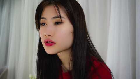 Media: Video of an East Asian woman with straight black hair, fair skin, and full lips, wearing a red top, set against a white curtain background.