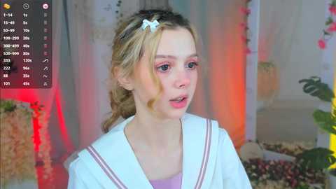 Media: Video of a young blonde girl in a sailor school uniform, standing indoors with a festive background, including a Christmas tree and potted plants.