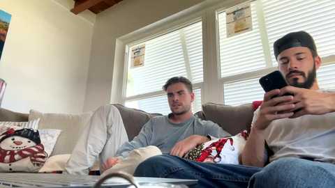 Media: Video of two men, one with a beard, on a beige sofa, reading newspapers, in a sunlit room with white blinds.