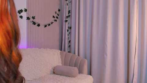 Media: Video of a cozy, softly lit room with a plush white couch, lavender curtains, and green ivy garland.