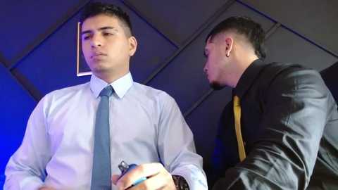 Media: Video of two men in suits, one with a blue tie, the other with a yellow tie, in a dimly lit office with blue lighting, looking serious and focused.