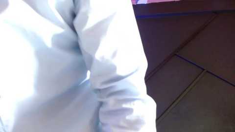 Media: A video showing a person in a white, long-sleeved shirt, captured from a low angle, with blurred background including a wooden ceiling and a red-painted wall.