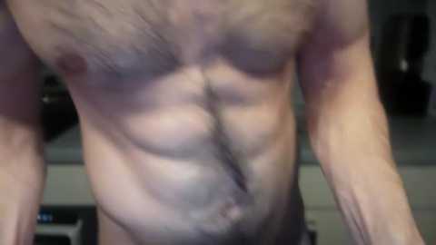 Media: A close-up video of a muscular, light-skinned man's torso with visible abs, chest hair, and a small, dark pubic patch. The background is blurry, possibly indoors with dim lighting.