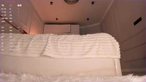 Media: A video of a modern, minimalist bedroom with a plush white bed covered in a striped blanket. The room features a white ceiling with recessed lighting and a white door on the right.