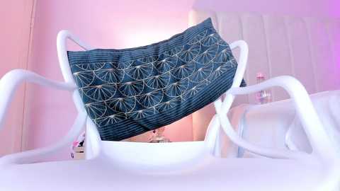 Media: Video of a white plastic chair with a blue denim mask featuring a geometric pattern, against a pink wall with a modern, minimalist interior.
