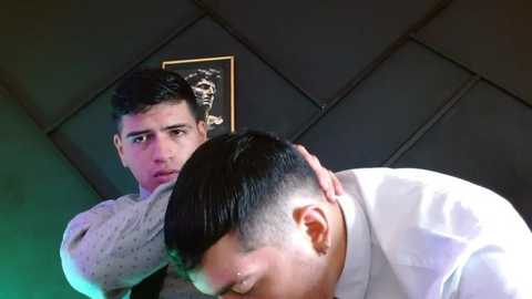 Media: Video of two young men in a dimly lit room; one has short dark hair, wearing a grey shirt, embraces another with short dark hair, wearing a white shirt.