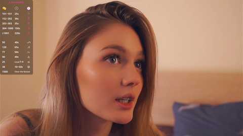 Media: Video of a young Caucasian woman with long, straight brown hair, wearing makeup, looking thoughtful, in a soft-lit indoor setting.