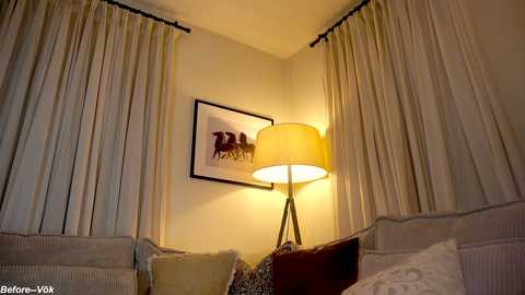 Media: A cozy corner of a hotel room with beige curtains, a framed artwork, a beige couch, and a warm-toned lamp with a cylindrical shade.